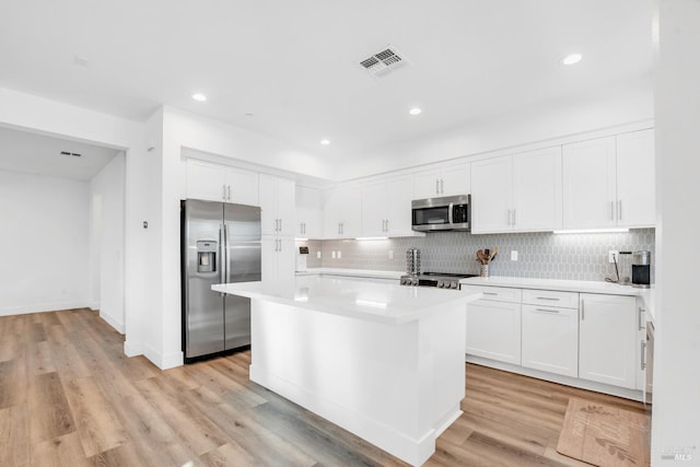 kitchen featuring stainless steel appliances, backsplash, white cabinets, a kitchen island, and light hardwood / wood-style flooring