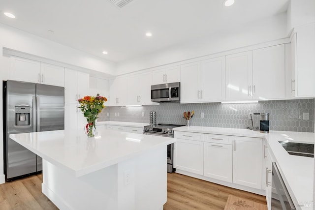 kitchen featuring stainless steel appliances, tasteful backsplash, white cabinets, a kitchen island, and light hardwood / wood-style flooring