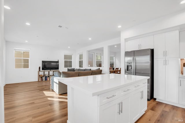 kitchen featuring white cabinetry, light hardwood / wood-style flooring, stainless steel fridge, and a kitchen island