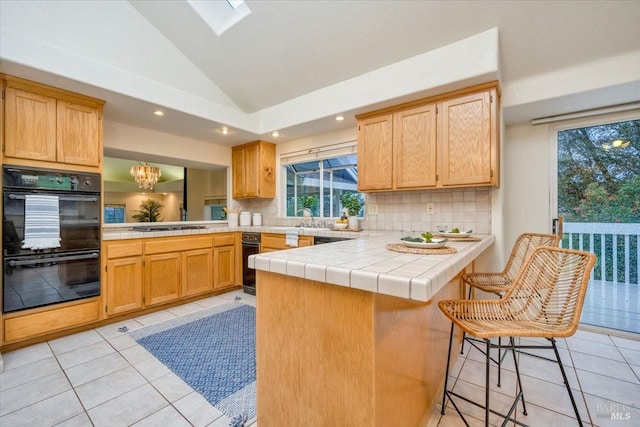 kitchen with backsplash, black appliances, kitchen peninsula, light tile patterned flooring, and a kitchen breakfast bar