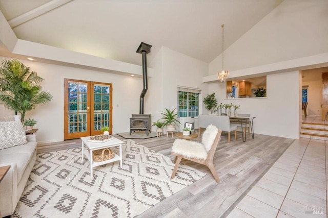 living room featuring a wealth of natural light, an inviting chandelier, a wood stove, high vaulted ceiling, and light tile patterned floors