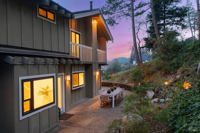 view of property exterior featuring outdoor dining area, a patio, a balcony, and board and batten siding