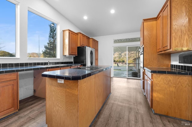 kitchen with black electric stovetop, wood-type flooring, stainless steel fridge, and a center island