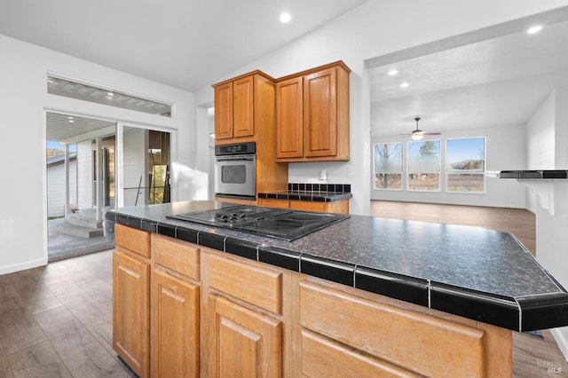 kitchen featuring a center island, tile counters, dark wood-type flooring, black electric stovetop, and stainless steel oven