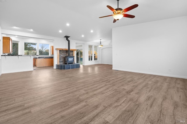 unfurnished living room featuring light wood-type flooring, ceiling fan, and a wood stove