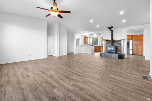 unfurnished living room featuring ceiling fan, a wood stove, and light hardwood / wood-style flooring