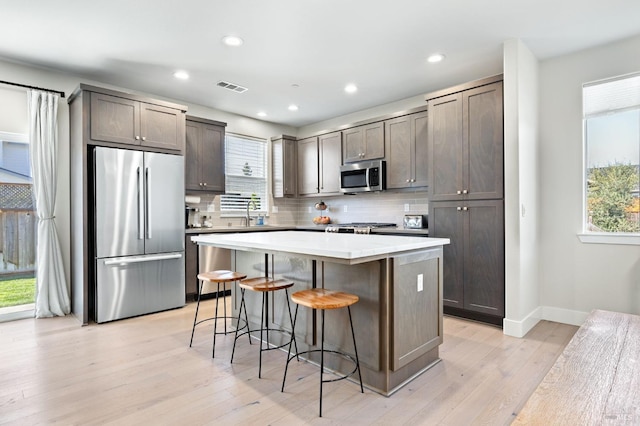 kitchen with appliances with stainless steel finishes, tasteful backsplash, light wood-type flooring, a wealth of natural light, and a center island