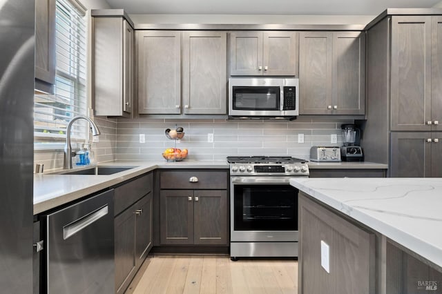 kitchen featuring light hardwood / wood-style floors, stainless steel appliances, tasteful backsplash, light stone countertops, and sink