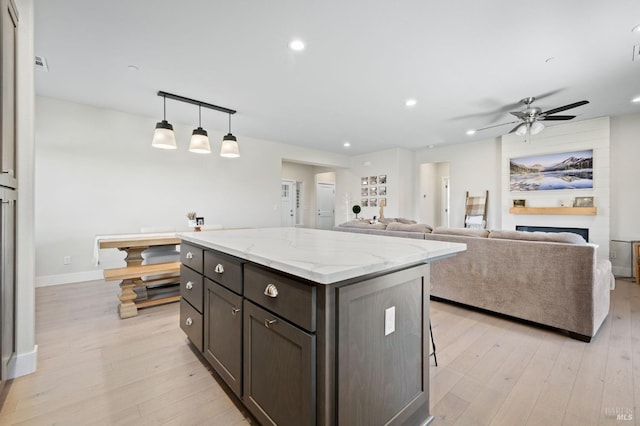 kitchen with ceiling fan, a fireplace, hanging light fixtures, dark brown cabinets, and light stone counters