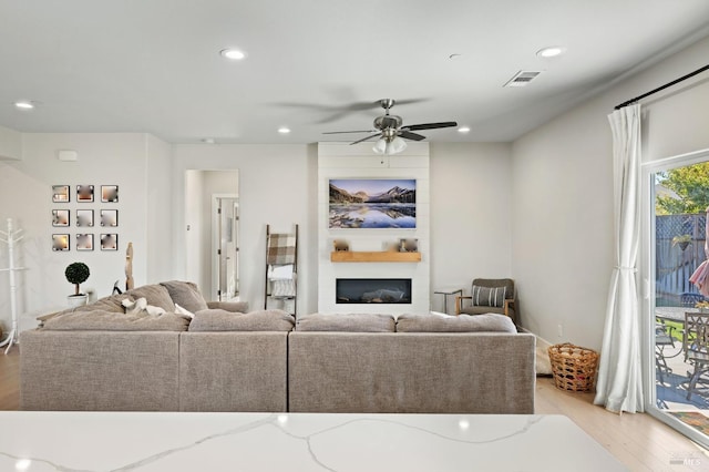 living room with ceiling fan, a large fireplace, and light hardwood / wood-style flooring