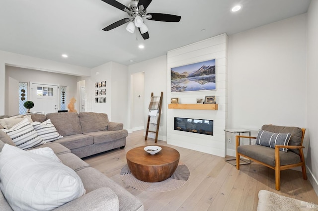 living room featuring ceiling fan, light wood-type flooring, and a fireplace