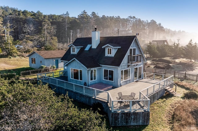 back of house featuring fence, a shingled roof, a deck, and a chimney