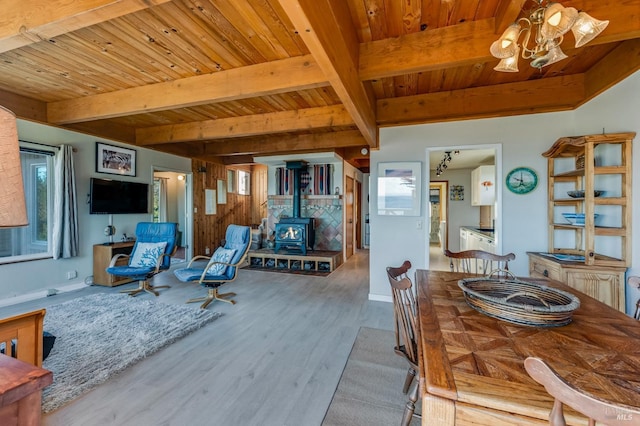 living room with beam ceiling, light hardwood / wood-style flooring, wood ceiling, a wood stove, and a chandelier