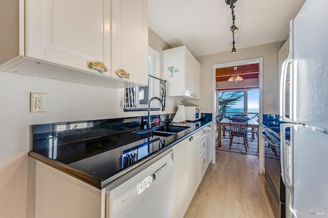 kitchen featuring sink, white appliances, light wood-type flooring, white cabinets, and dark stone counters