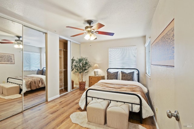 bedroom featuring ceiling fan, multiple closets, light wood-type flooring, and a textured ceiling