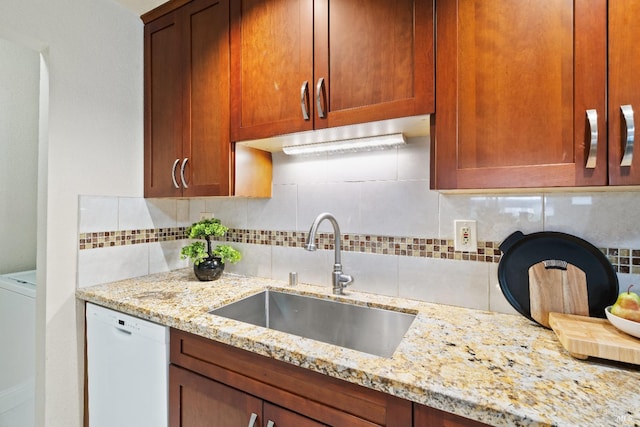 kitchen with backsplash, washer / dryer, sink, white dishwasher, and light stone countertops