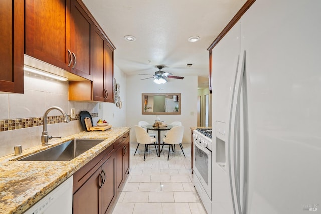 kitchen featuring ceiling fan, decorative backsplash, sink, white appliances, and light stone counters