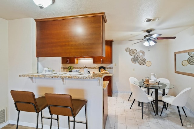 kitchen with a kitchen breakfast bar, ceiling fan, a textured ceiling, and kitchen peninsula