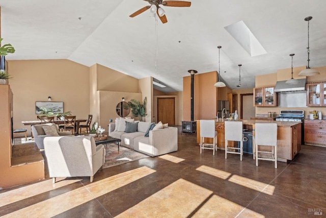 living room featuring high vaulted ceiling, a wood stove, ceiling fan, and a skylight