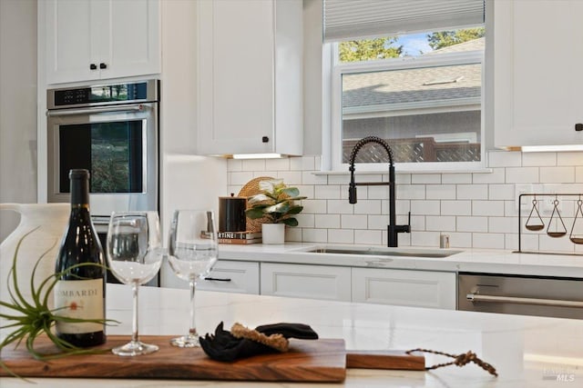 kitchen featuring stainless steel appliances, white cabinetry, light stone countertops, and sink