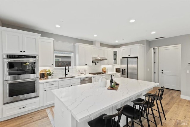 kitchen with a kitchen island, sink, white cabinets, light stone counters, and stainless steel appliances