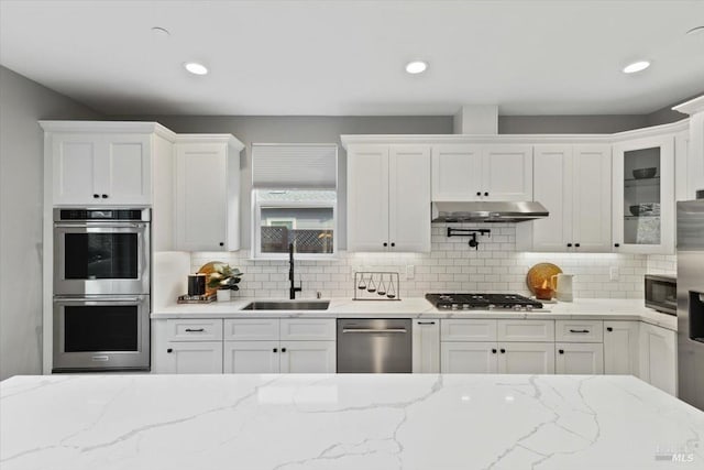 kitchen with white cabinetry, appliances with stainless steel finishes, sink, and light stone counters