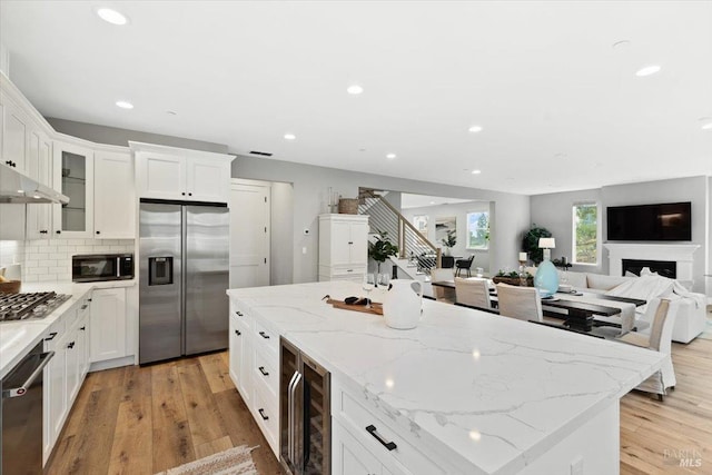 kitchen with light stone counters, white cabinetry, beverage cooler, and appliances with stainless steel finishes