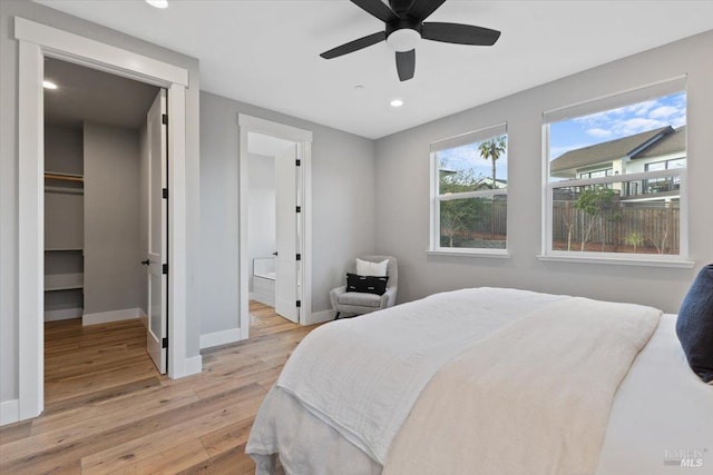 bedroom featuring ceiling fan, a walk in closet, connected bathroom, and light hardwood / wood-style floors