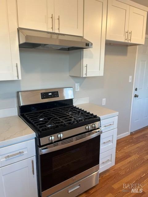 kitchen with under cabinet range hood, light wood-style floors, white cabinetry, baseboards, and gas stove