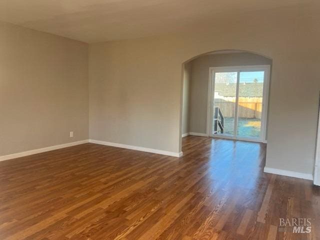 unfurnished room with dark wood-type flooring, baseboards, and arched walkways