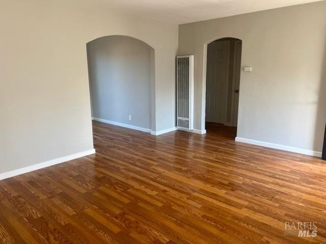 empty room featuring a heating unit, wood finished floors, baseboards, and arched walkways