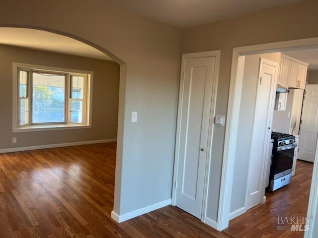 corridor with dark wood-style flooring, baseboards, and arched walkways