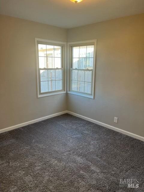 spare room with dark colored carpet and baseboards