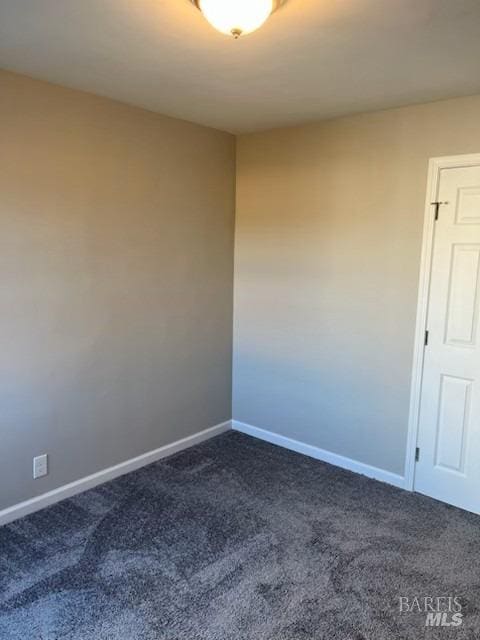 spare room featuring dark colored carpet and baseboards