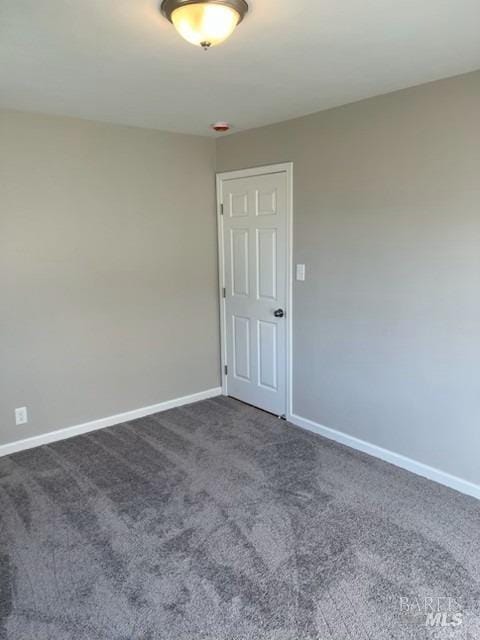 spare room featuring dark carpet and baseboards