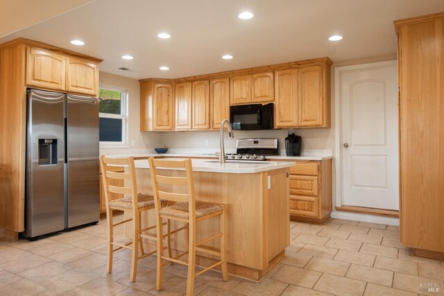 kitchen with appliances with stainless steel finishes, a kitchen bar, a center island with sink, and light brown cabinets