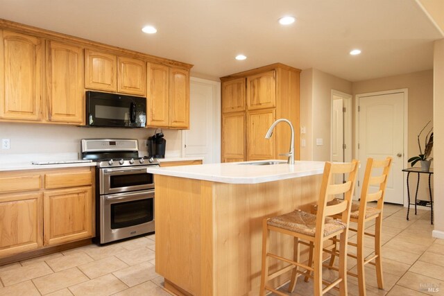 kitchen with sink, a breakfast bar area, range with two ovens, light tile patterned floors, and a center island with sink