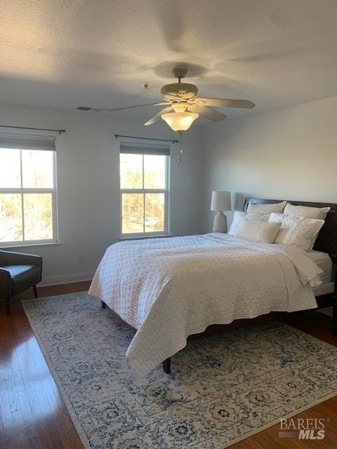 bedroom with ceiling fan, multiple windows, and dark hardwood / wood-style flooring