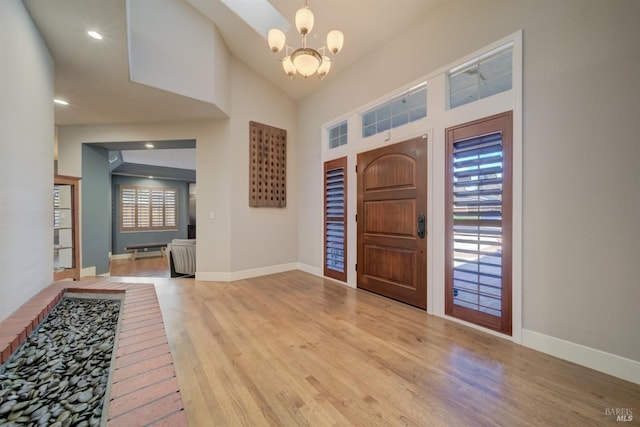 foyer with light wood-type flooring, high vaulted ceiling, and an inviting chandelier