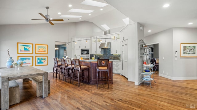 kitchen featuring white cabinetry, a skylight, built in appliances, backsplash, and a breakfast bar area