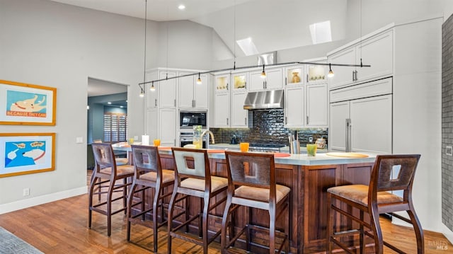 kitchen with backsplash, built in appliances, hanging light fixtures, and an island with sink