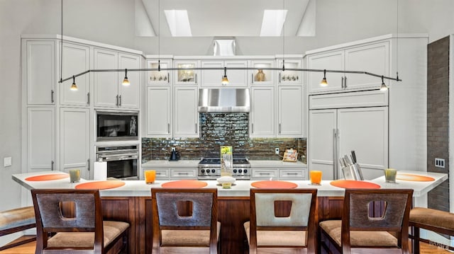 kitchen featuring built in appliances, a kitchen bar, decorative backsplash, pendant lighting, and a center island with sink