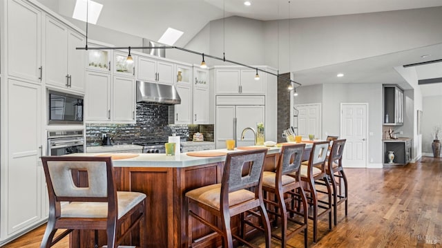 kitchen featuring high vaulted ceiling, pendant lighting, built in appliances, and an island with sink