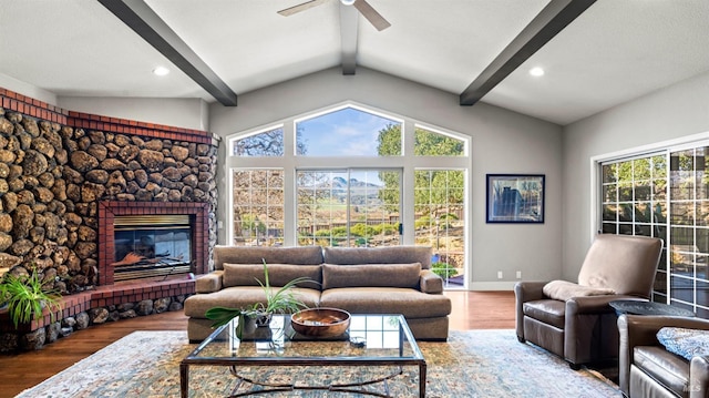 living room featuring wood-type flooring, lofted ceiling with beams, a stone fireplace, and ceiling fan