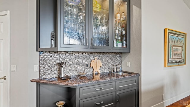 bar featuring tasteful backsplash, sink, dark stone countertops, dark hardwood / wood-style floors, and gray cabinets