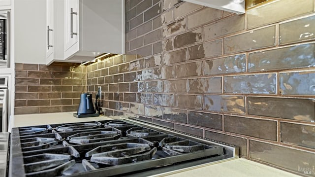 details featuring decorative backsplash, stovetop, and white cabinetry