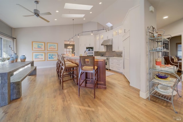 kitchen with tasteful backsplash, white cabinets, black microwave, pendant lighting, and an island with sink