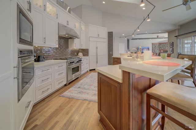 kitchen with a large island with sink, white cabinets, stainless steel appliances, decorative backsplash, and a breakfast bar area