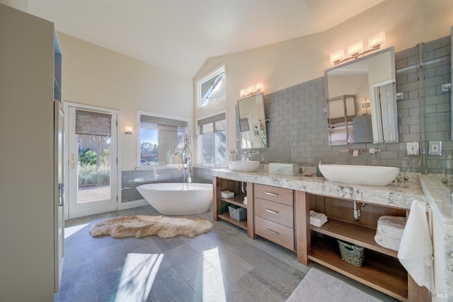 bathroom with vanity, vaulted ceiling, a tub to relax in, and tasteful backsplash