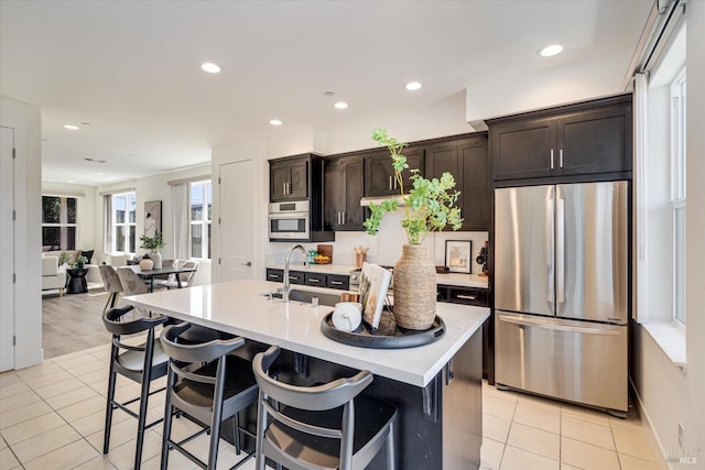 kitchen featuring a center island with sink, a breakfast bar, dark brown cabinetry, stainless steel appliances, and light tile patterned floors